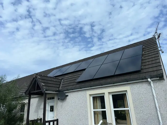 Black solar panels across the roof of a house under a blue sky